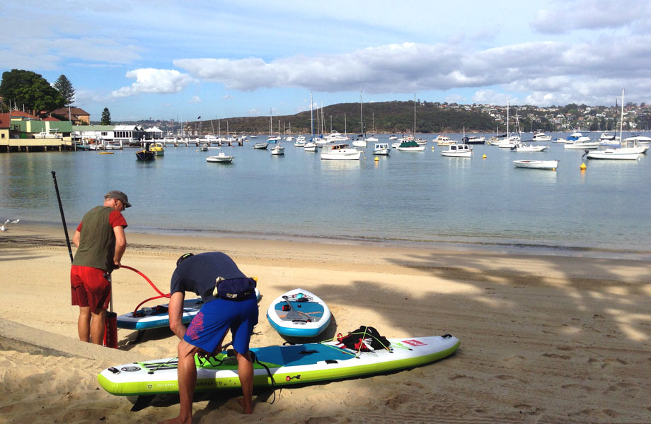two men pump up there paddle boards on beach