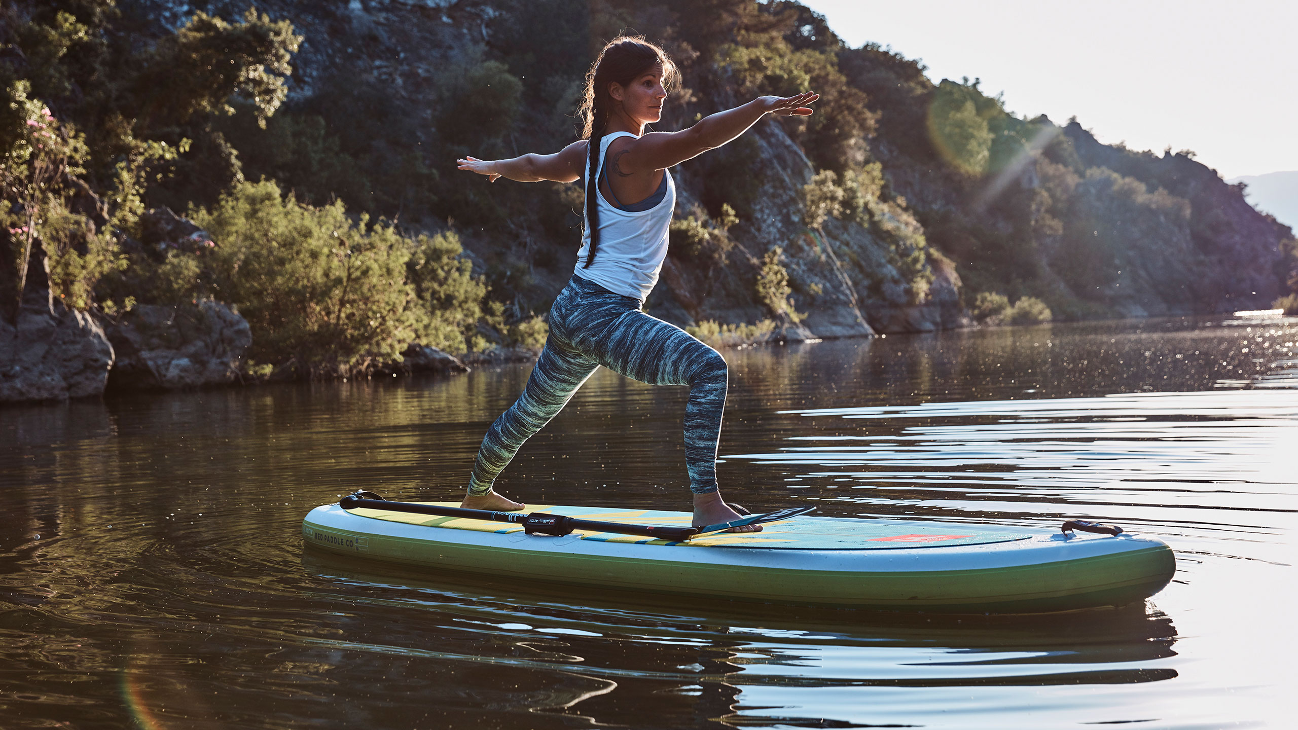 woman stands and holds yoga pose on paddle board