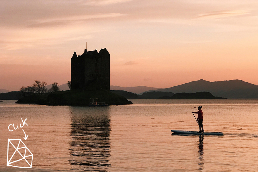 woman paddles past castle at sunset in Scotland 