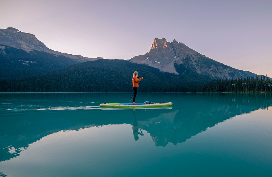 Girl stands on paddle board on glassy still lake