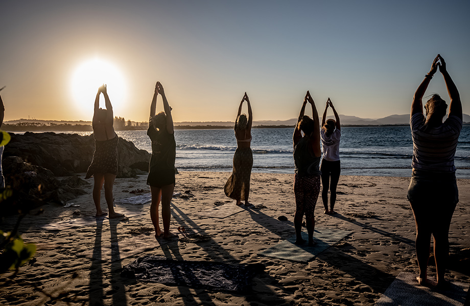 Group of women practicing yoga on the beach at sunrise