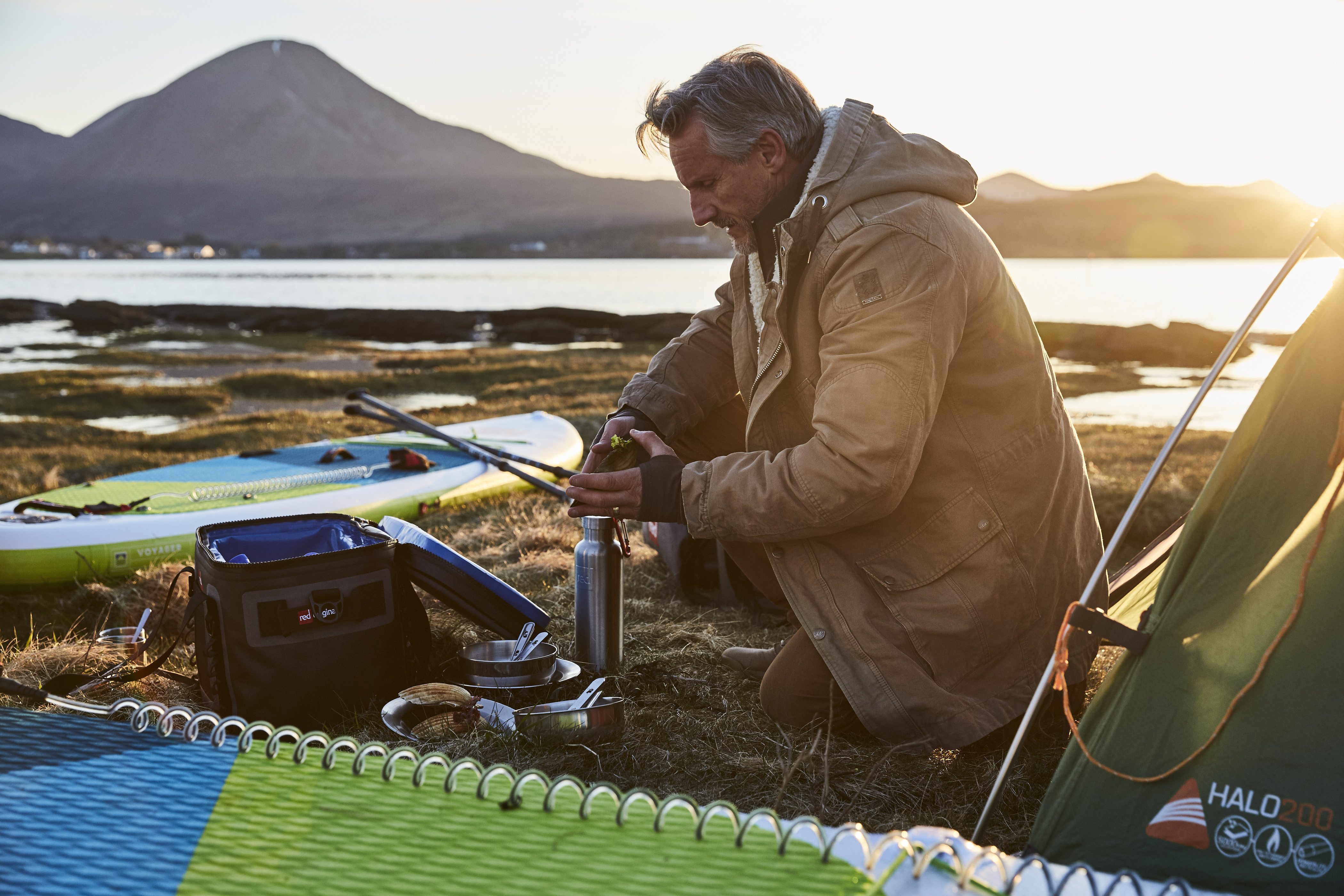A man surrounded by camping equipment and inflatable paddle boards warms up