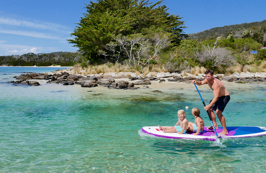 Man paddle boarding with two children on the front