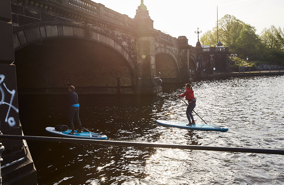 Couple paddle towards bridge on inflatable paddle boards