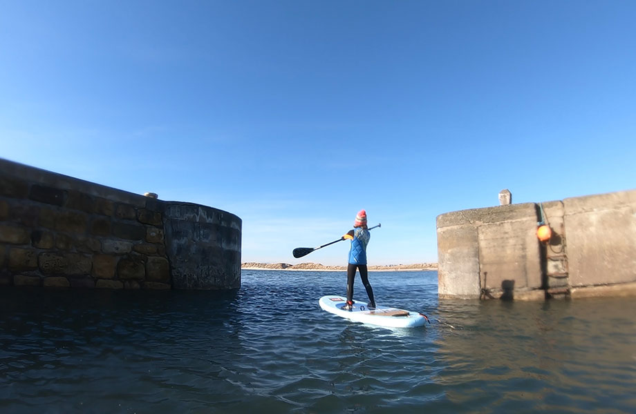 Child paddles on SUP with bobble hat in winter