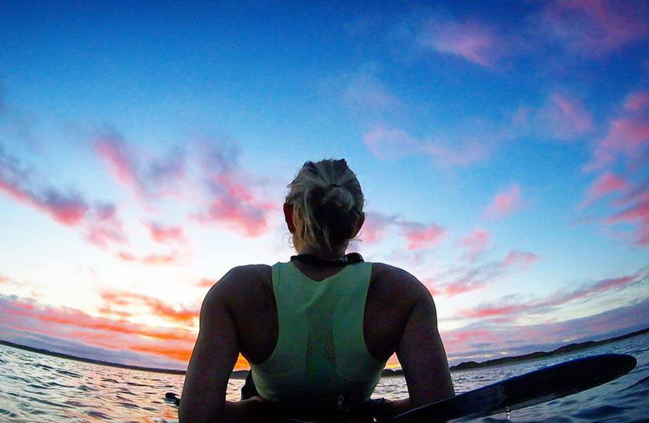 Woman looks out a sunset on her paddle board at sea