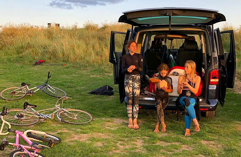 Kids sit in back of van and eat snacks in their wetsuits