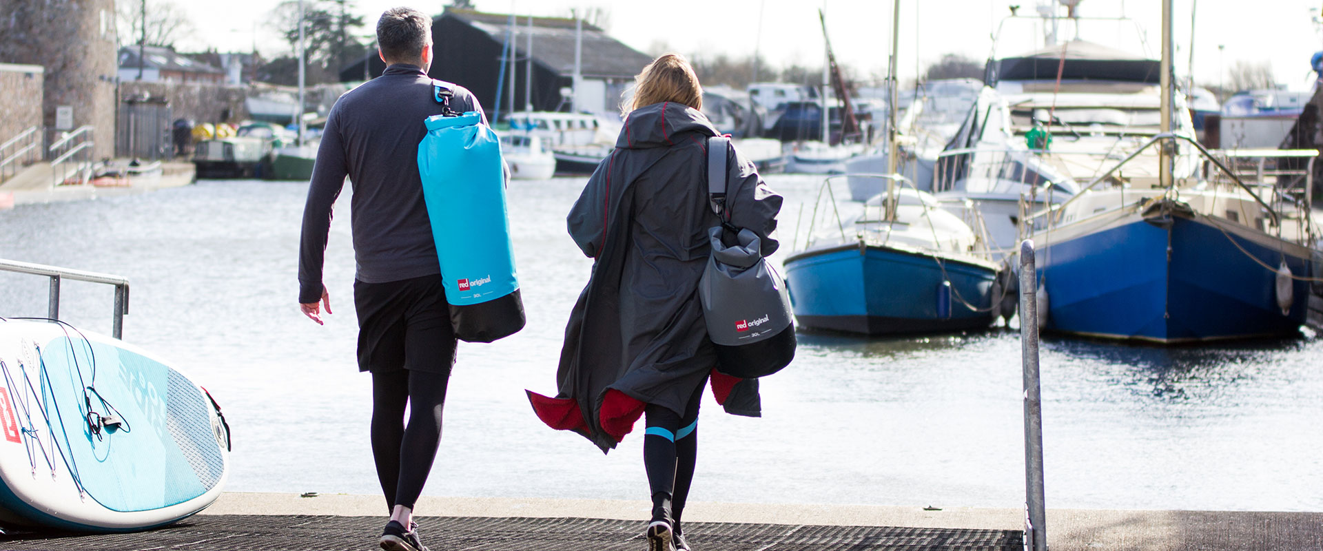 couple walk towards the water carrying Red Original dry bags
